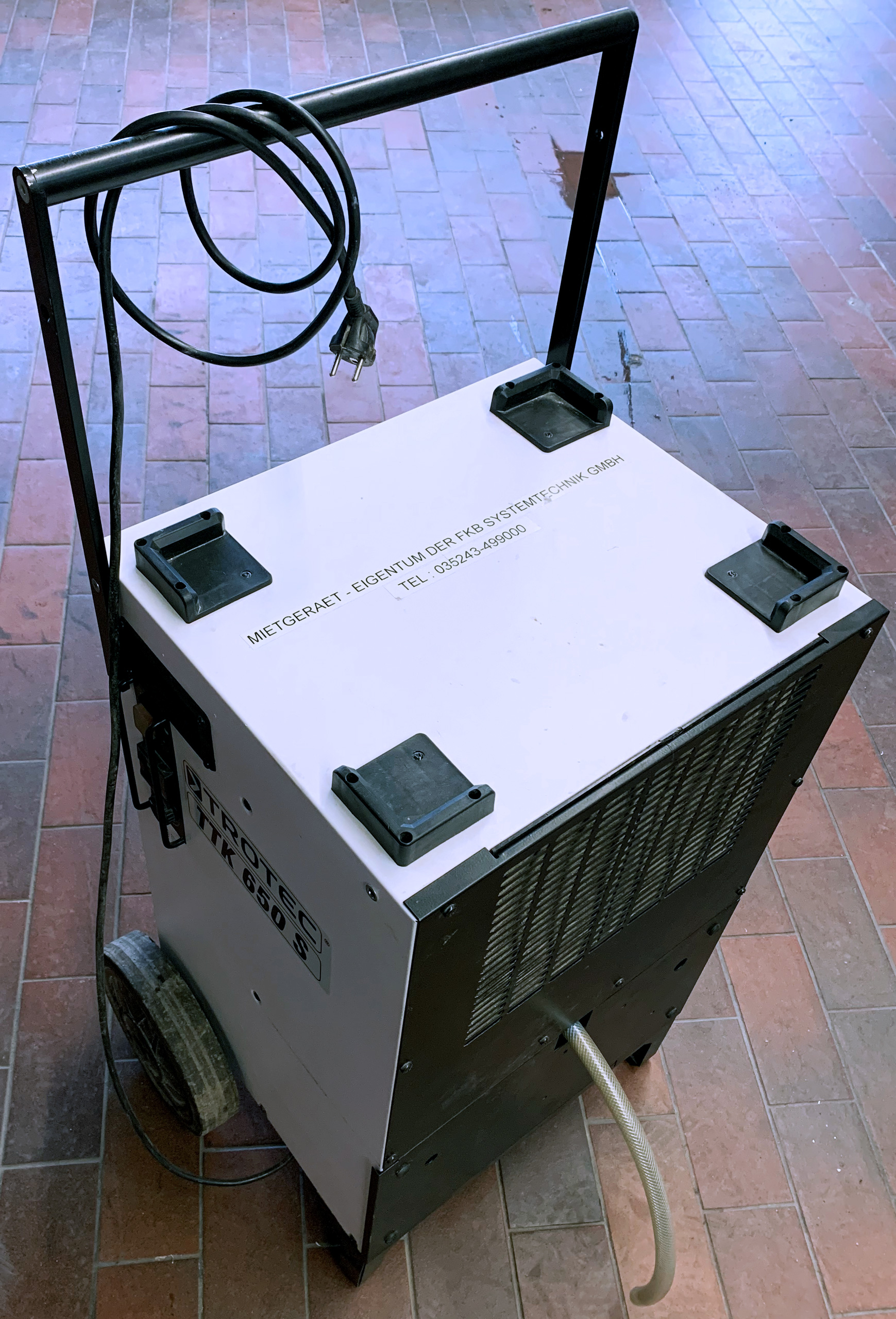 Oberansicht des Leihgeräts Luftentfeuchter TTK 650 S mit aufgerolltem Stromkabel und Ablassschlauch